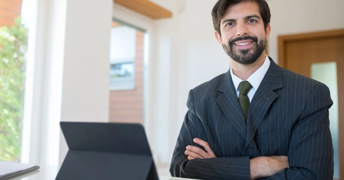 Homme d'affaires professionnel souriant dans un bureau avec une tablette, habillé en costume et cravate.