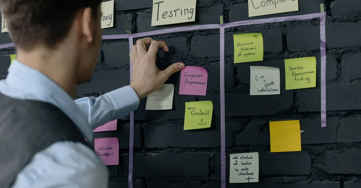 Homme organisant des tâches de projet sur un mur avec des notes autocollantes dans un bureau moderne.