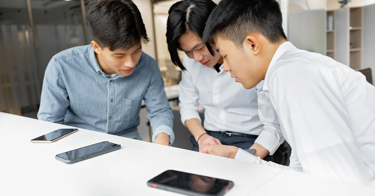 Trois collègues en pleine réflexion dans un bureau moderne, concentrés sur leurs smartphones.