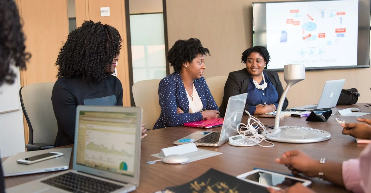 Quatre femmes diverses engagées dans une réunion d'affaires avec des ordinateurs portables et des présentations dans un bureau.