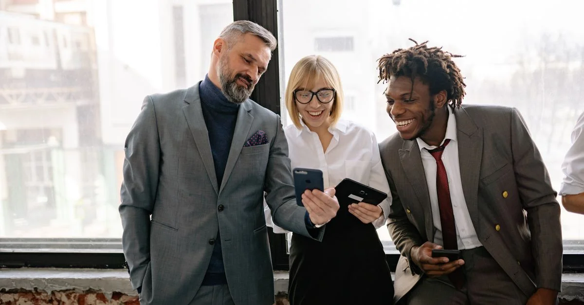 Trois collègues dans un bureau moderne partageant un moment sur leurs smartphones.