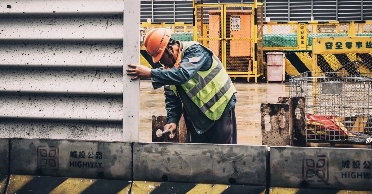 Un ouvrier du bâtiment en gilet réfléchissant et casque de sécurité sur un chantier urbain animé.