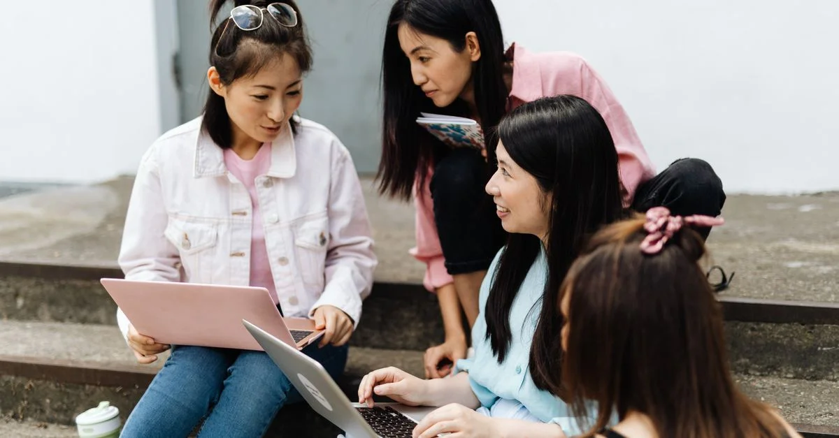 Quatre femmes collaborant à l'extérieur sur des ordinateurs portables, montrant le travail d'équipe et l'interaction.