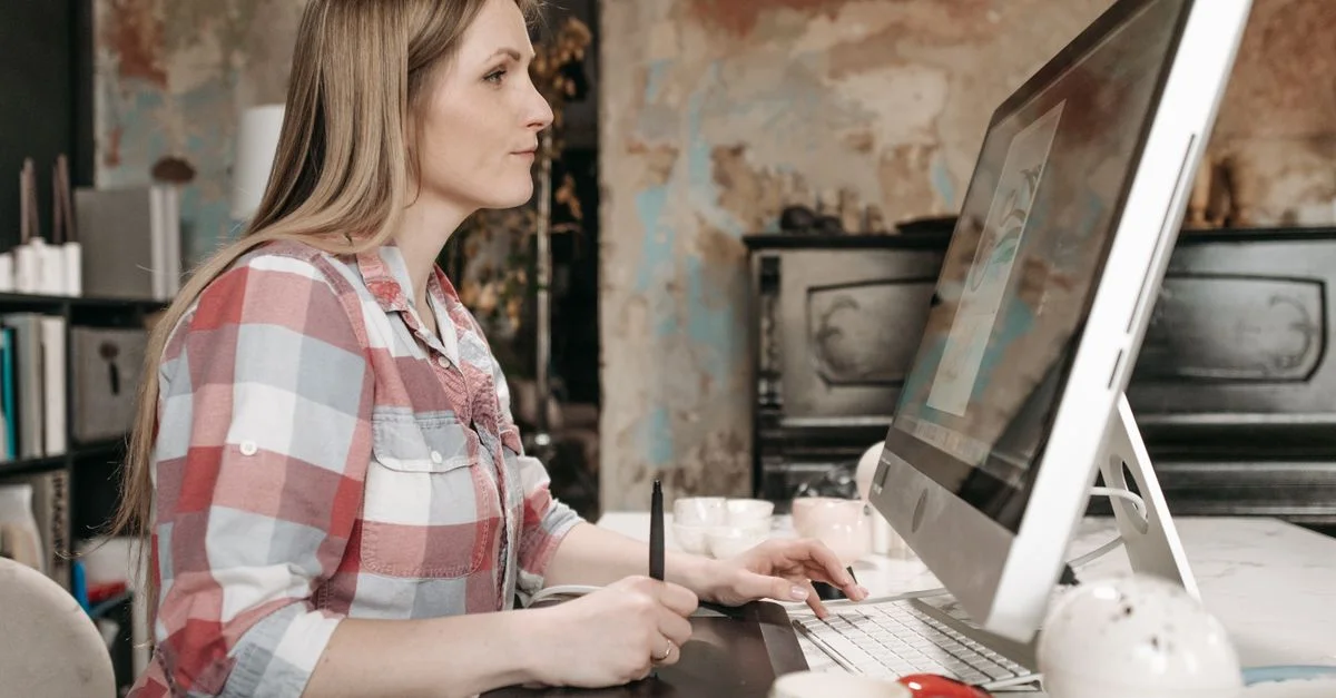 Vue de côté d'une femme utilisant une tablette graphique devant un ordinateur dans un bureau élégant.