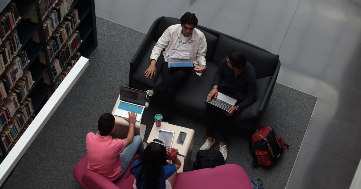 Un groupe d'adultes divers collaborant sur des ordinateurs portables dans un espace lounge de la bibliothèque.