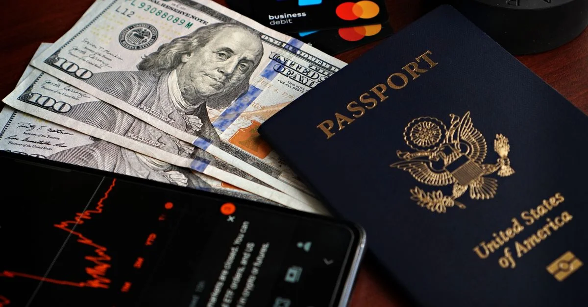 Passeport américain avec billets de cent dollars, cartes de crédit et smartphone affichant des données boursières.