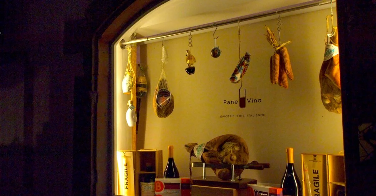 Vitrine chaleureuse d'une épicerie italienne présentant vins, fromages et charcuteries.