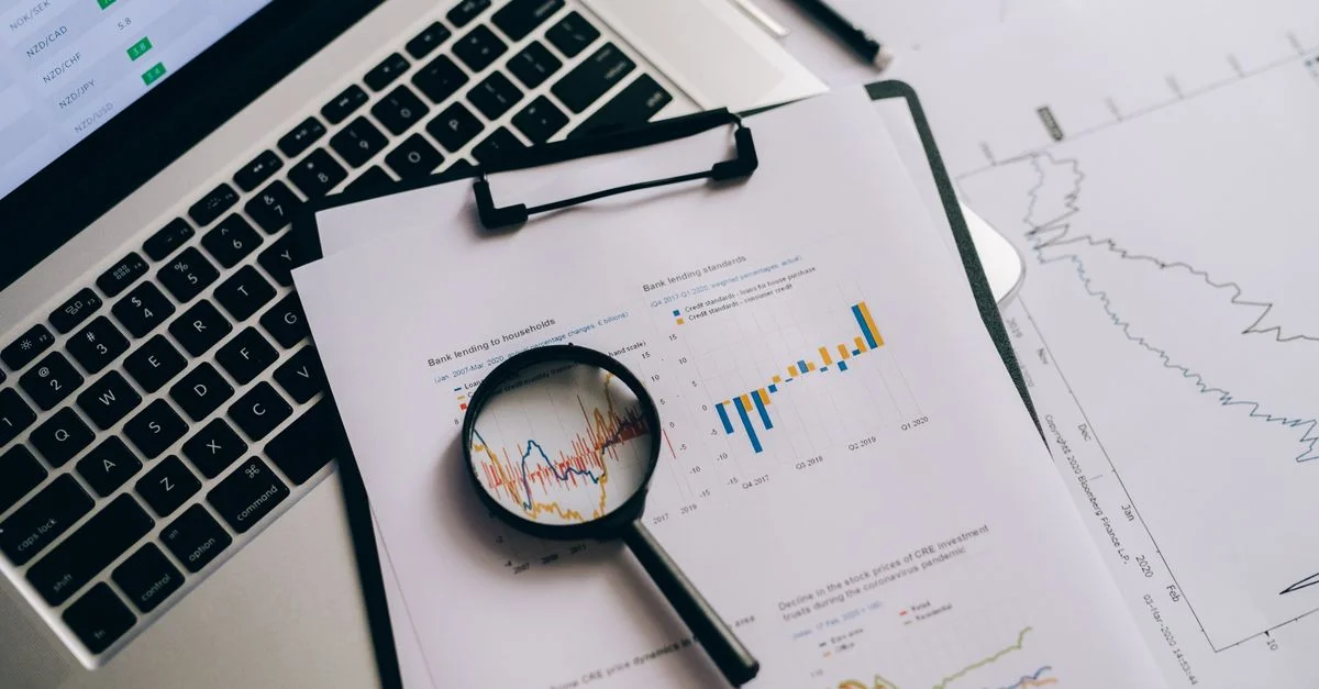 Vue de dessus des graphiques financiers, d'un ordinateur portable et d'une loupe, idéal pour des thèmes d'analyse commerciale.