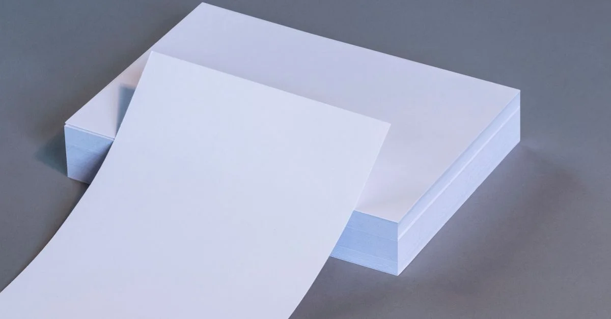 Une image de haute qualité montrant des feuilles de papier blanc vierge empilées sur une surface grise neutre.