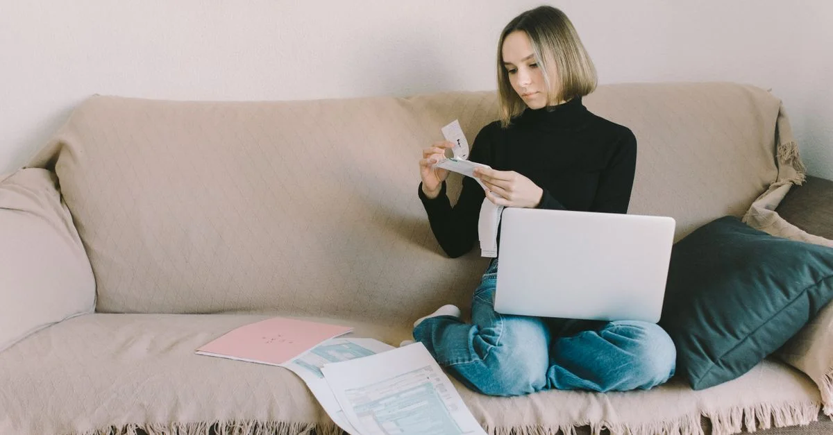 Une femme travaillant depuis chez elle sur un canapé avec un ordinateur portable et des documents, gérant ses finances.