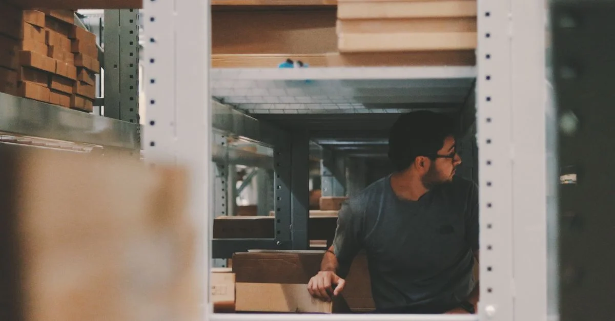 Homme organisant des planches en bois sur des étagères d'entrepôt, créant une solution de stockage efficace.